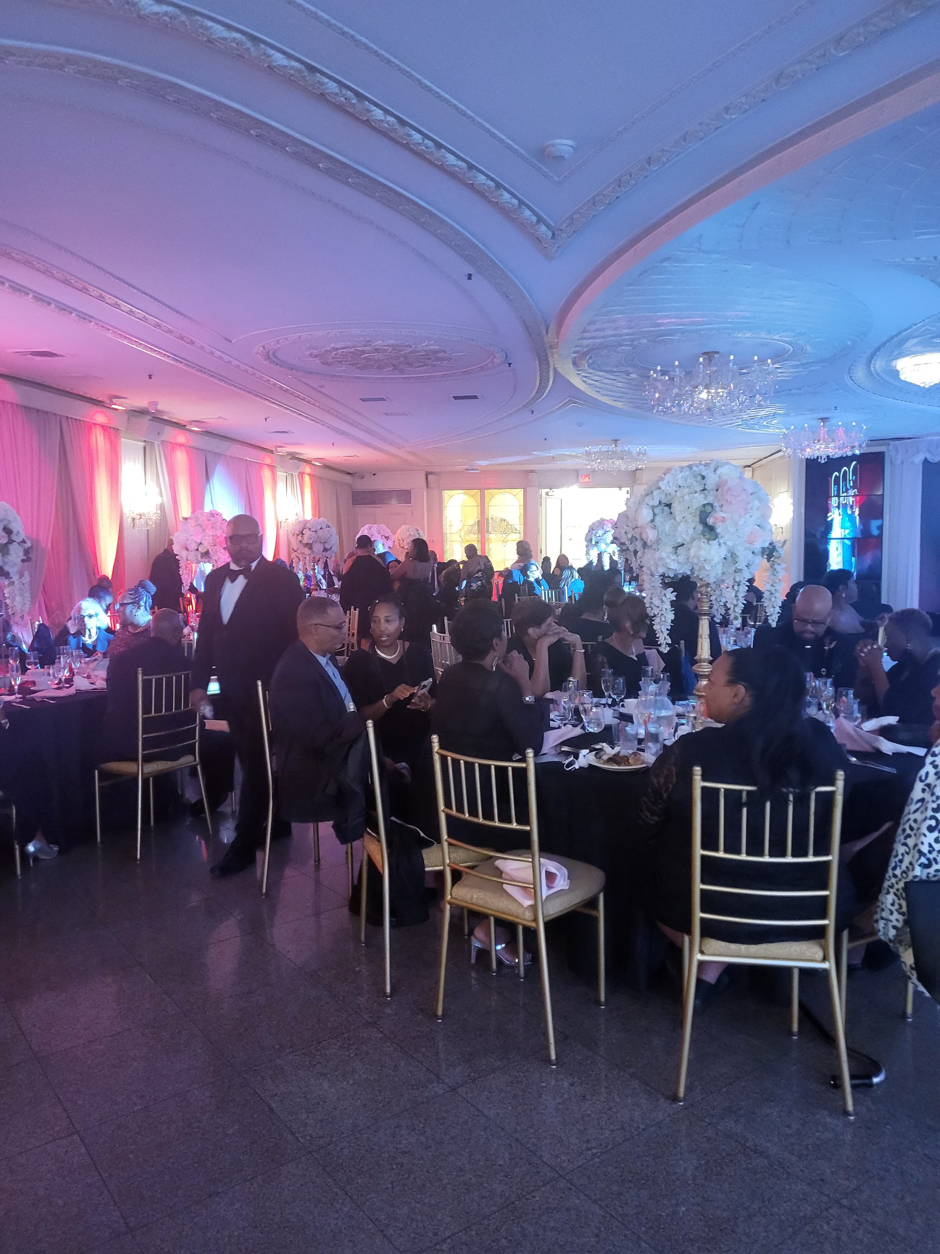 Guests seated at a formal ballroom dinner with tall floral centerpieces